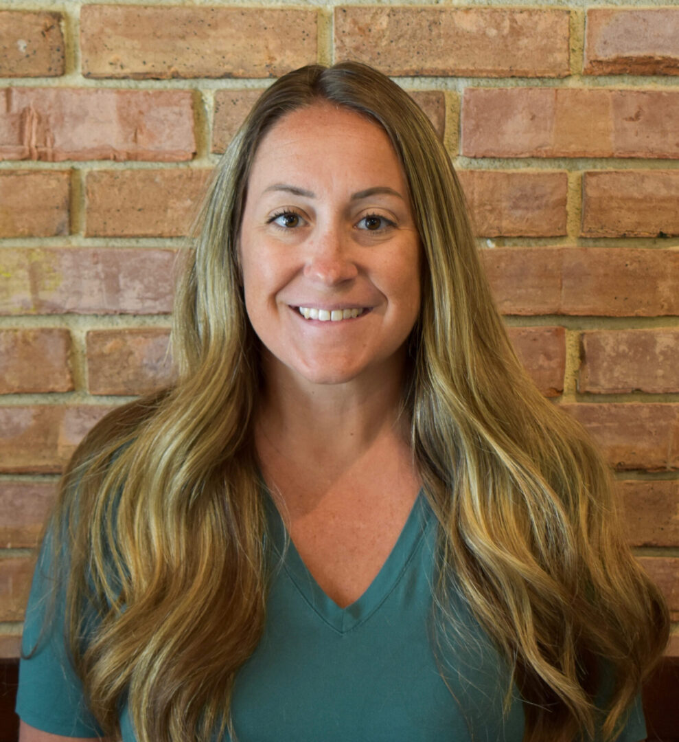 A woman with long hair standing in front of a brick wall.